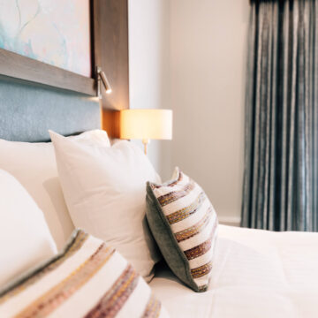 Cozy hotel room with plush bedding, striped cushions, elegant curtains, and warm ambient lighting for a relaxing stay.