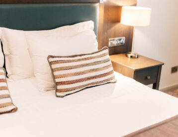 Cosy hotel room with plush pillows, a stylish bedside lamp, and soft ambient lighting for a relaxing stay.