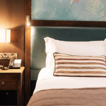 Cosy hotel room with elegant decor, plush bedding, bedside lamp, and phone, offering comfort and relaxation for guests.