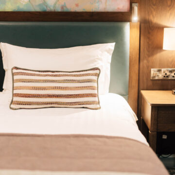 Cosy hotel room with plush bed, striped pillow, warm lighting, and floral artwork, ideal for relaxing stays.