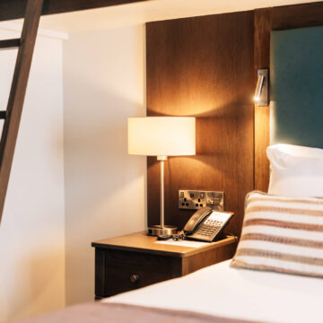 Elegant hotel room with cozy bed, plush pillows, stylish nightstand, and warm lighting. Ideal for a relaxing getaway.