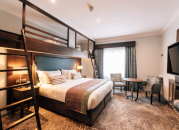 Stylish hotel room with plush double bed, loft bunk bed, cosy seating area, flat-screen TV, and modern decor.