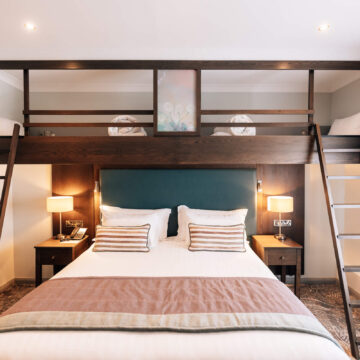 Elegant hotel room with double bed, cosy lighting, loft storage, bedside lamps, and plush bedding for a relaxing stay.