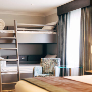 Cosy hotel room with bunk beds, plush chair, ambient lighting, and modern decor ideal for families or groups.