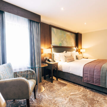 Cozy hotel room with plush bed, elegant décor, natural light, seating area, and soft lighting for a relaxing stay.