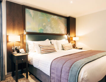 Stylish hotel room with king-sized bed, soft lighting, cosy pillows, and modern decor for a relaxing stay.