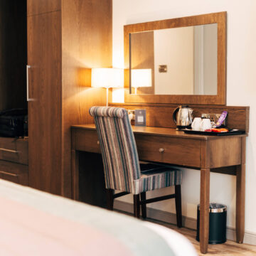 Stylish hotel room with striped chair, large mirror, tea-making facilities, warm lighting, spacious wardrobe. Relaxing stay.