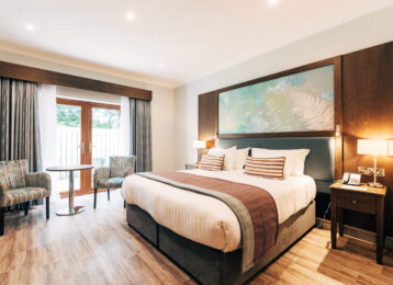 Modern hotel room with king-size bed, artwork, patio doors, seating area, and soft lighting; perfect for relaxation.