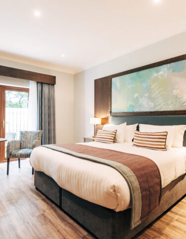 Modern hotel room with king-size bed, artwork, patio doors, seating area, and soft lighting; perfect for relaxation.