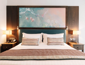 Elegant hotel room with plush double bed, artistic headboard, bedside lamps, and modern amenities for a cosy stay.