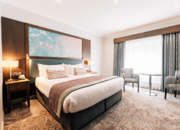 Spacious hotel room with king-size bed, cosy armchairs, and large window, offering a relaxing retreat for guests.