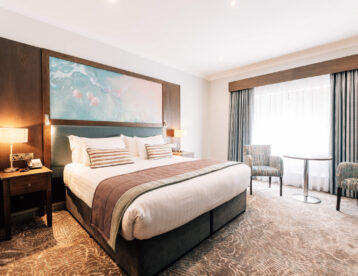 Spacious hotel room with king-size bed, cosy armchairs, and large window, offering a relaxing retreat for guests.