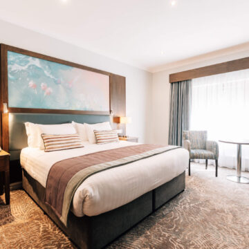 Spacious hotel room with king-size bed, cosy armchairs, and large window, offering a relaxing retreat for guests.