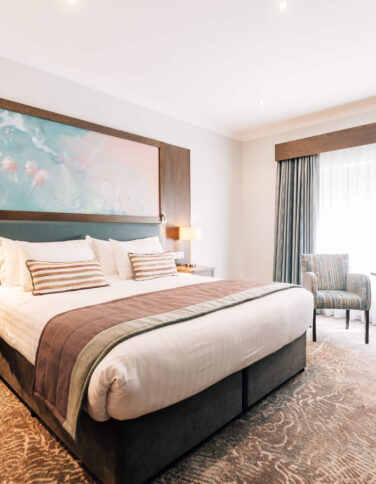 Spacious hotel room with king-size bed, cosy armchairs, and large window, offering a relaxing retreat for guests.
