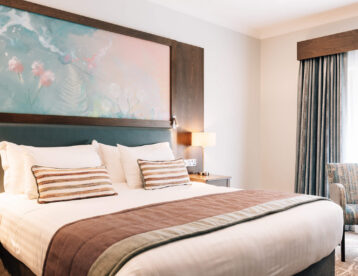 Stylish hotel room with cosy king-sized bed, soft lighting, modern artwork, and elegant drapes creating a relaxing atmosphere.