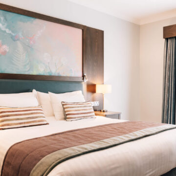Stylish hotel room with cosy king-sized bed, soft lighting, modern artwork, and elegant drapes creating a relaxing atmosphere.