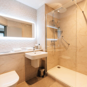 Luxurious hotel bathroom with walk-in rain shower, illuminated mirror, and modern amenities for a relaxing stay.
