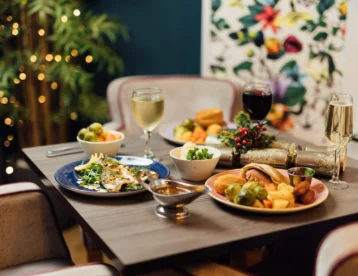 Cosy hotel dining with fine wine and gourmet meal set on an elegant table with colourful decor and glowing fairy lights.