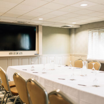 Bright meeting room with large TV, elegant table setup, and comfortable seating for business or events in a welcoming hotel.