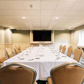 Bright hotel conference room with elegant seating, long table, large screen, ideal for meetings and events.