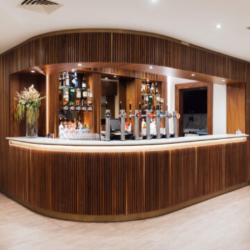 Elegant hotel bar with modern wood panelling, ambient lighting, and top-shelf spirits; perfect for relaxing evening drinks.
