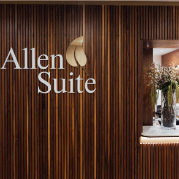 Elegant hotel lobby with wooden decor, Allen Suite logo, and welcoming floral arrangement