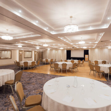 Elegant hotel event space with round tables, chandeliers, and modern decor, ideal for conferences and weddings.